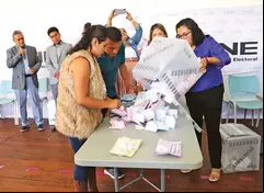 Funcionarios de casilla vaciando una urna en un simulacro de conteo de votos.